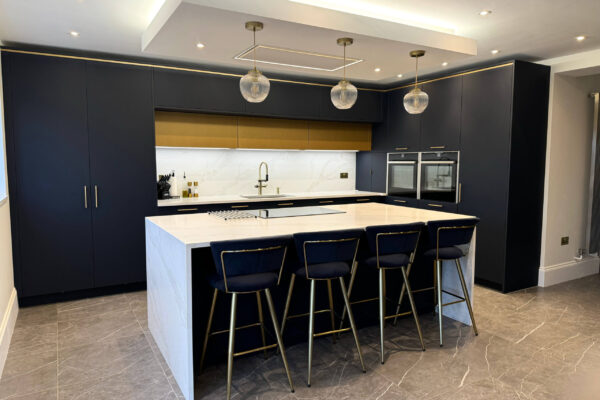 Elegant navy blue kitchen in Harpenden featuring quartz worktops, a waterfall island and integrated NEFF appliances
