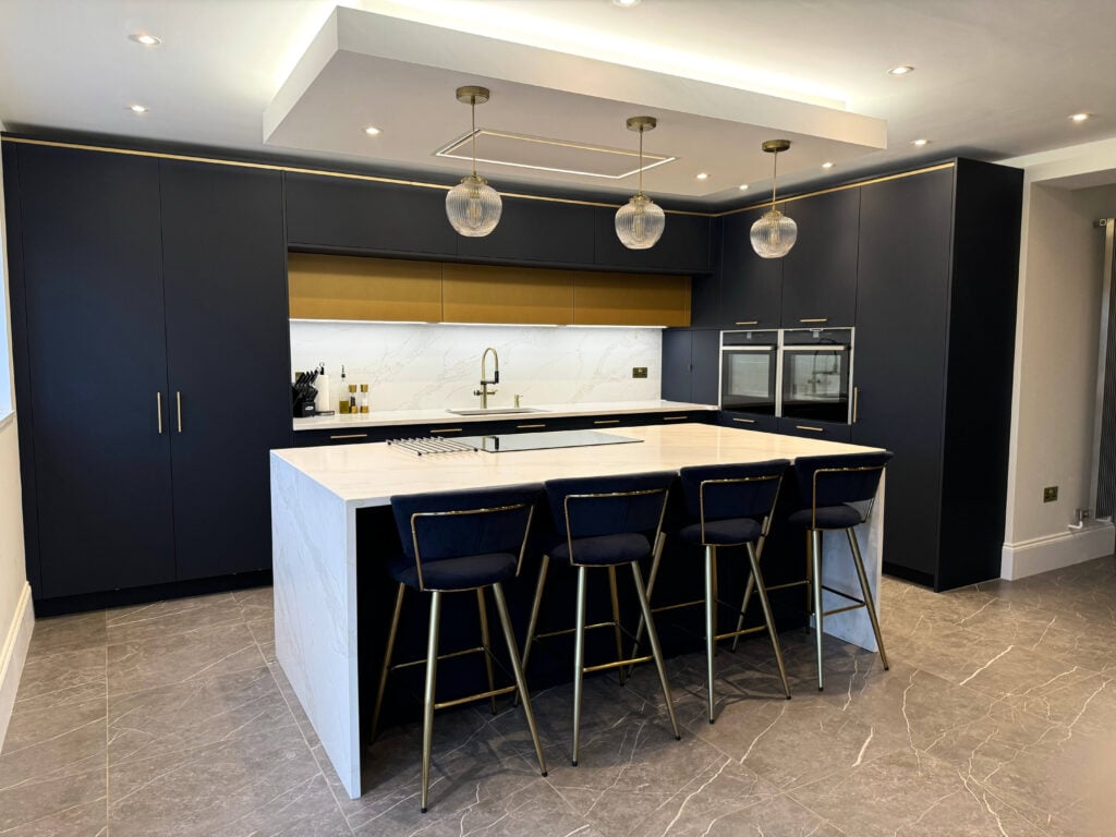 Elegant navy blue kitchen in Harpenden featuring quartz worktops, a waterfall island and integrated NEFF appliances